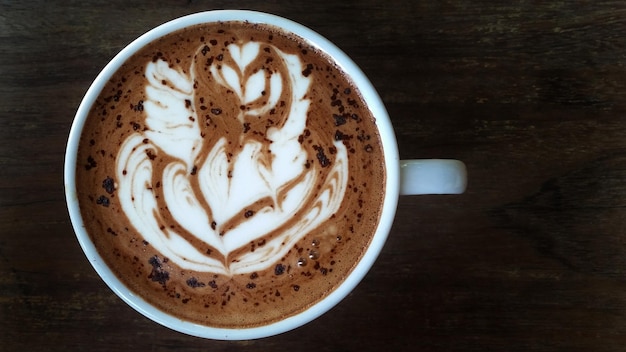 Vista directamente por encima del capuchino con arte de espuma servido en una mesa de madera