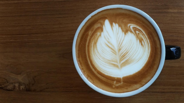 Vista directamente por encima del capuchino con arte de espuma servido en una mesa de madera