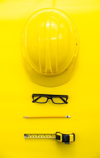 Foto vista directamente por encima del casco con gafas y lápiz con cinta métrica sobre fondo amarillo