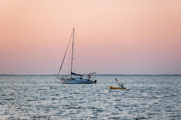 Vista distante do homem no barco de cor amarela perto do iate que está no mar