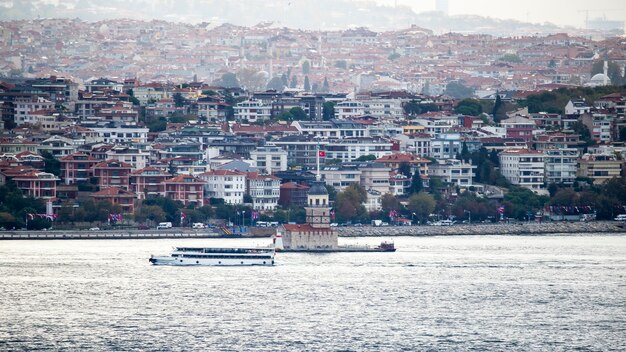 Vista de un distrito con modernos edificios residenciales en Estambul, Estrecho del Bósforo con la torre de Leander y barco en movimiento en primer plano, Turquía