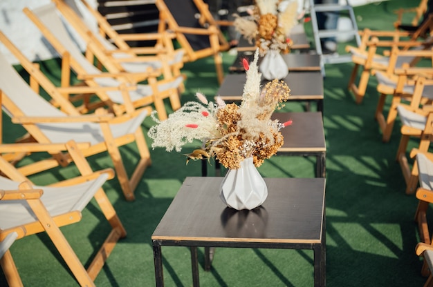 Vista do aconchegante café ao ar livre no telhado. mesa com espreguiçadeiras de madeira. há um vaso decorativo com flores secas na mesa