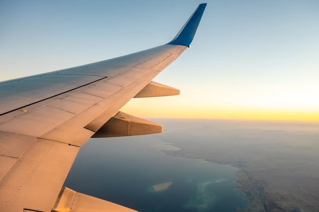 Vista do avião na asa branca da aeronave voando sobre a paisagem do oceano em uma manhã ensolarada