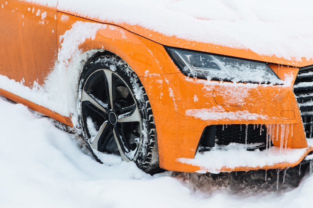 Vista do carro laranja coberto de neve, fica na estrada, congelada na geada