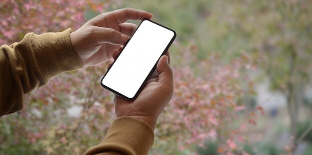 Vista do close-up de jovem segurando o smartphone de tela em branco