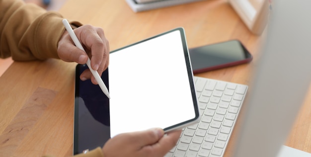 Vista do close-up de jovem trabalhando em seu projeto com tablet de tela em branco