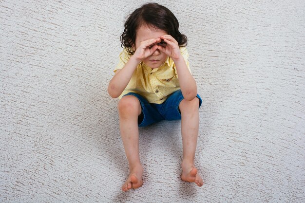 Foto vista do menino bonitinho pensativo cobrindo os olhos