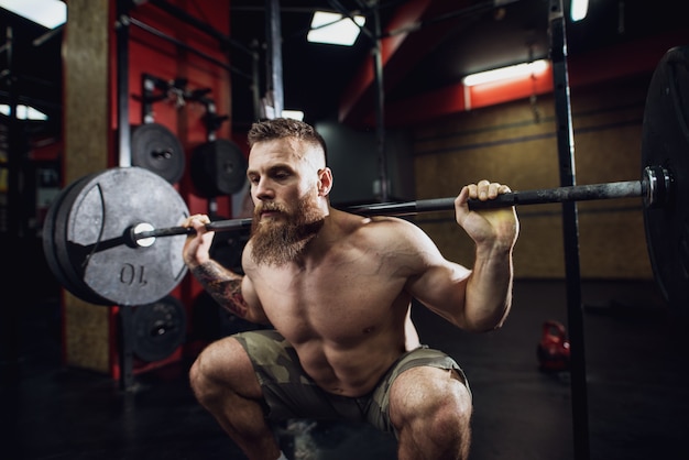 Vista do retrato do jovem barbudo homem forte aptidão muscular focado agachado