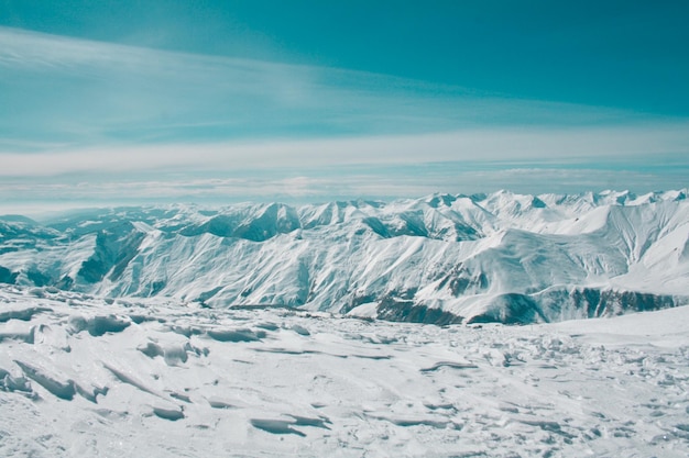 Vista do topo da montanha em picos cobertos de neve no céu azul ciano Gudauri Georgia Daylight com nuvens Paisagem idílica