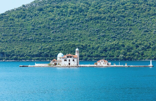 Vista do verão na ilha artificial com a Igreja Católica Romana de Nossa Senhora das Rochas. Construído em 1632y. (Cidade de Perast, Montenegro, baía de Kotors)