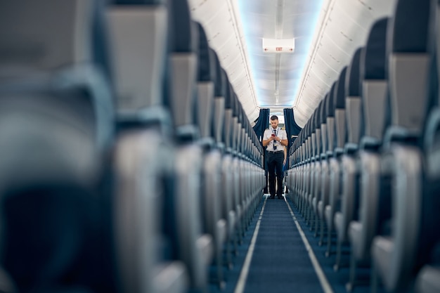 Vista dos assentos do passageiro da linha aérea na cabine do avião enquanto o homem está de pé no topo do corredor