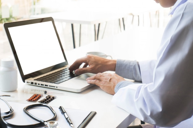 Vista dos detalhes das mãos do médico digitando no teclado com tela em branco.