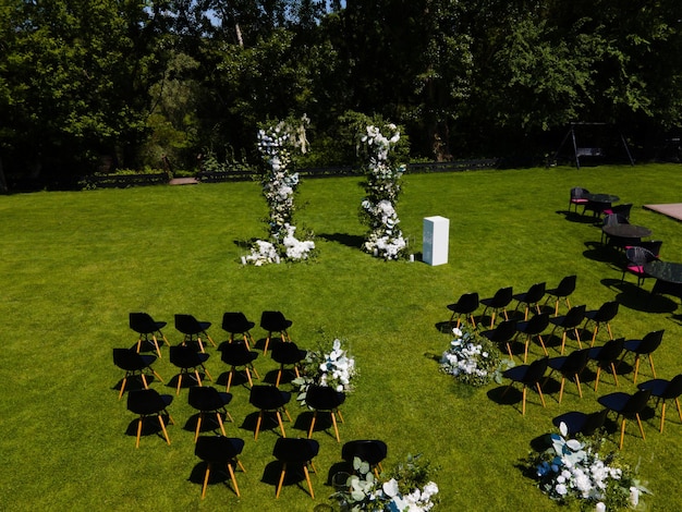 Vista desde el dron en la ceremonia de la boda en el césped con el arco de la boda y sillas para los invitados