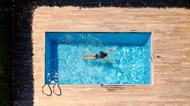 Vista de dron en toda su longitud de una mujer irreconocible con cabello oscuro largo y húmedo flotando en una piscina al aire libre en un día soleado en un complejo tropical