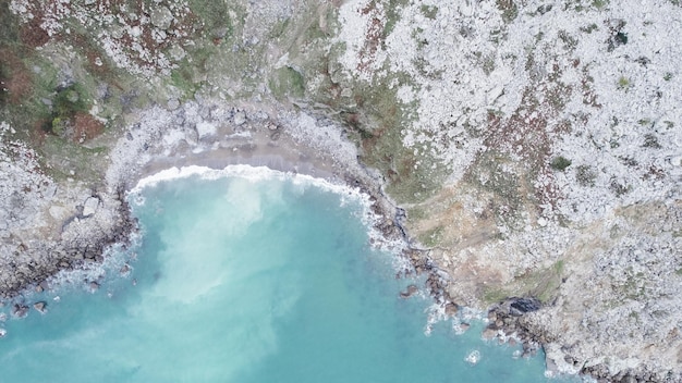 Vista por drones de la costa de lavado de agua turquesa del océano con olas espumosas rodeadas por un enorme acantilado rocoso ubicado en Cantabria España