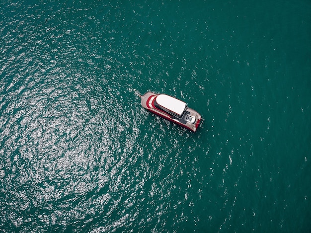 Vista de drones de la pequeña y nueva lancha motora roja y blanca en el mar azul, brilla bajo el sol brillante; concepto de buques.