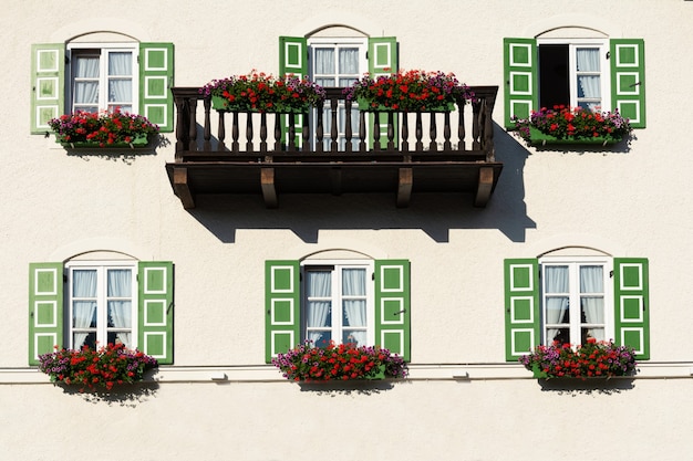 Foto vista del edificio con balcón y ventanas con persianas verdes decoradas con flores.