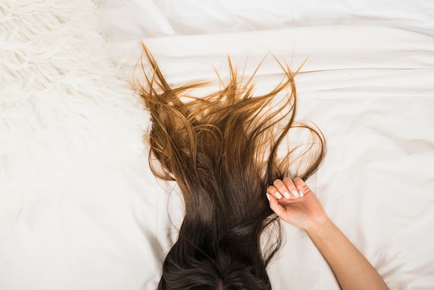 Una vista elevada del cabello de una mujer tendida en la cama blanca.