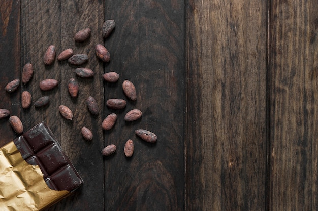 Foto vista elevada de granos de cacao tostados y barra de chocolate en la mesa de madera