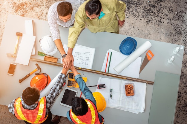 Vista em alto ângulo de arquitetos do sexo masculino empilhando as mãos sobre a mesa