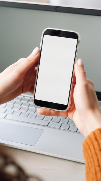 Vista por encima del hombro de una mujer sosteniendo un teléfono móvil con una pantalla celular simulada en blanco en blanco