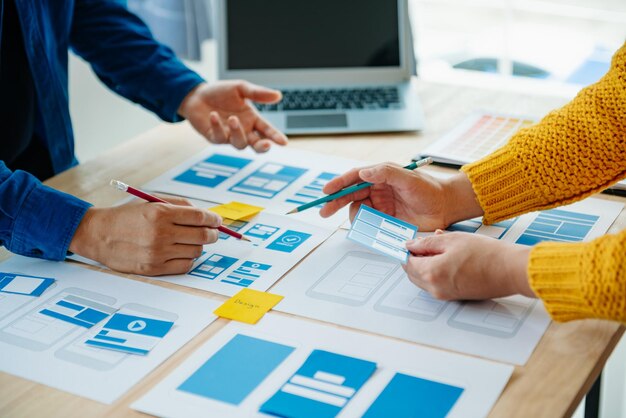 Vista del equipo de desarrolladores de la interfaz de usuario haciendo una lluvia de ideas sobre su proyecto con un teléfono inteligente portátil y una tableta digital Agencia de desarrollo digital creativaxA