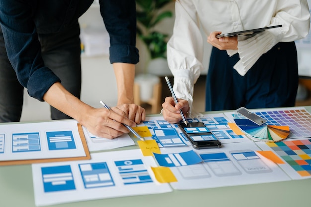 Vista del equipo de desarrolladores de la interfaz de usuario haciendo una lluvia de ideas sobre su proyecto con un teléfono inteligente portátil y una tableta digital Agencia de desarrollo digital creativaxA