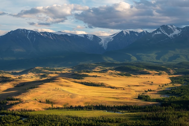 Vista escénica soleada al valle del bosque con río serpenteante contra alta cordillera nevada a la luz del sol. Hermoso río de montaña de serpientes en bosques y montañas nevadas bajo un cielo espectacular.