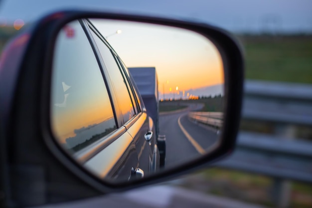 Vista en el espejo lateral de un coche en movimiento en la carretera y la puesta de sol en el cielo