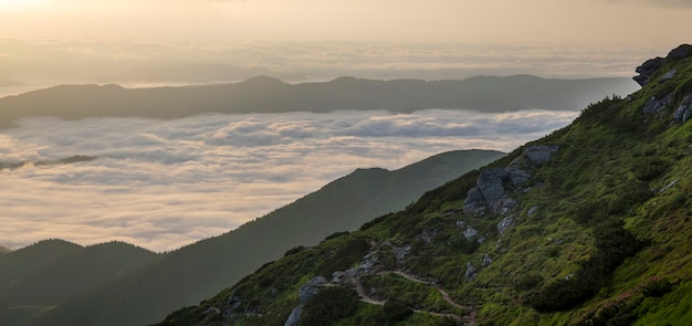 Foto vista fantástica do vale da montanha coberta com baixo branco inchado como nuvens de neve, estendendo-se para o horizonte nebuloso sob o céu brilhante da manhã com brilho laranja claro ao nascer do sol. beleza do conceito de natureza.