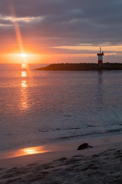 Foto vista del faro de punta carola y la playa durante una puesta de sol rojiza