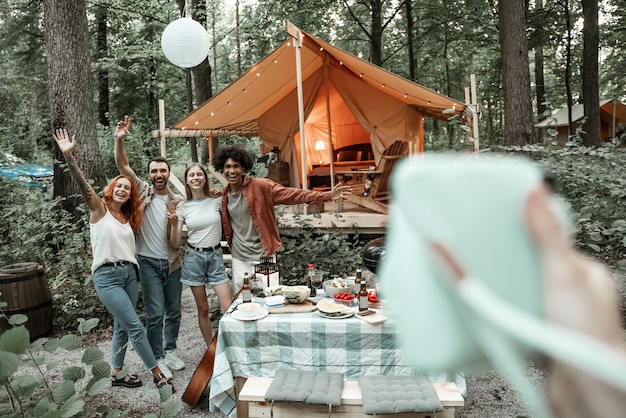 Vista del fotógrafo de hacer una foto polaroid de amigos en un picnic, acampar en la vida glamping, descansar con diversos amigos al aire libre, disfrutar de un viaje de campamento de verano, divertirse en el bosque, espacio de copia