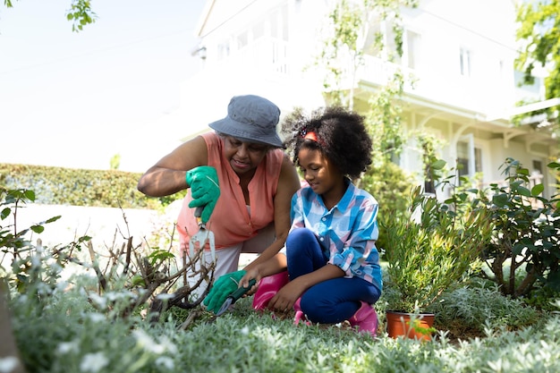 Vista frontal de una abuela afroamericana con su nieta en el jardín, arrodillada y cultivando juntos. Familia disfrutando del tiempo en casa, concepto de estilo de vida