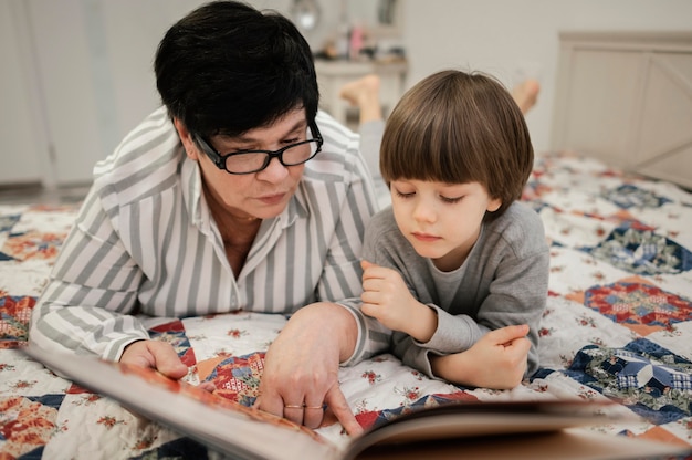Vista frontal de la abuela y el nieto en casa leyendo juntos