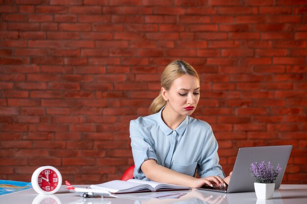 Vista frontal de la agencia de viajes sentada detrás de su lugar de trabajo y usando la computadora portátil gerente de ocupación en el interior de la agencia asistente servicio de turismo global