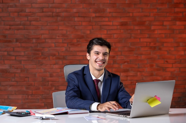 Vista frontal del agente de viajes sentado detrás de su lugar de trabajo en traje y usando una computadora portátil Agencia de ocupación corporativa Proyecto de turismo en el extranjero Asistente global