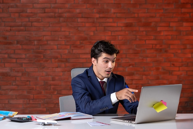 Vista frontal del agente de viajes sentado detrás de su lugar de trabajo en traje y usando una computadora portátil Servicio de ocupación corporativa Turismo en el extranjero Proyectos de asistente de la agencia global