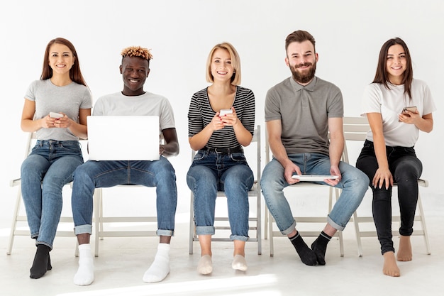 Foto vista frontal amigos sentados em cadeiras com dispositivos modernos