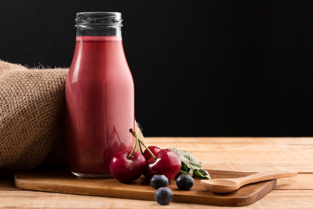 Vista frontal de arándanos y cerezas con batido en botella de vidrio