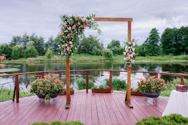 Vista frontal del arco de madera minimalista decorado con flores y vegetación se encuentra en el fondo del lago