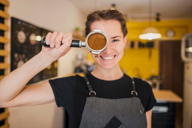 Vista frontal de la barista femenina posando con la taza de la máquina llena de café