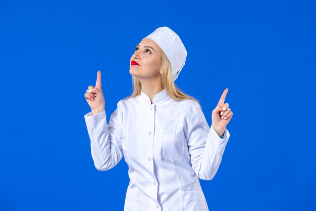 Vista frontal de la bonita enfermera en traje médico sobre fondo azul enfermedad hospitalaria covid- medicina de salud enfermedad por virus pandémico