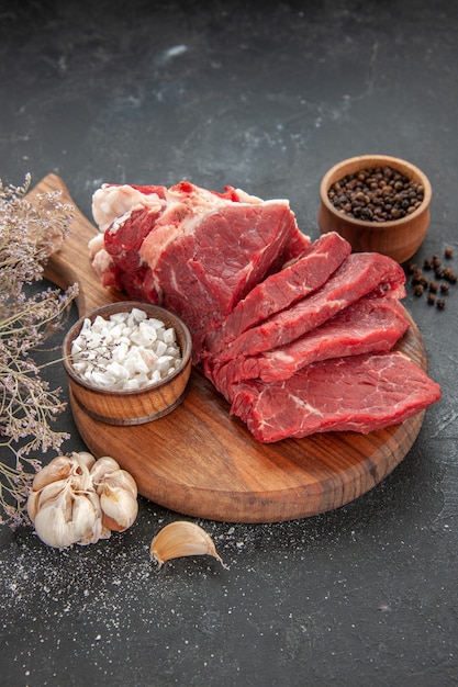 Vista frontal de carne fresca en rodajas con ajo y pimienta sobre fondo oscuro carne comida comida animal barbacoa color carnicero cena