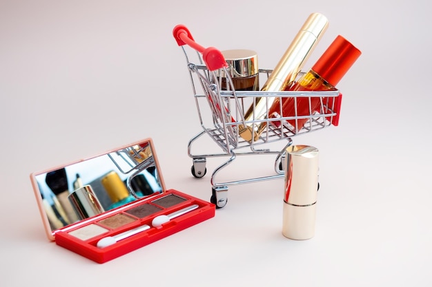 Vista frontal de un carrito de compras con productos de maquillaje en un fondo rosa Concepto de compras cosméticas