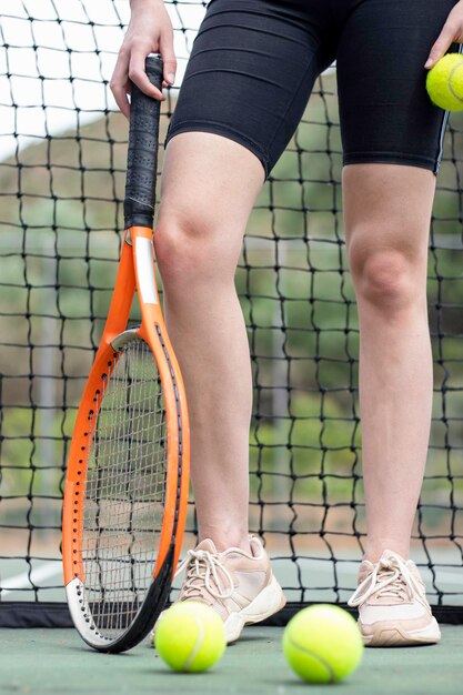 Foto vista frontal de cerca de las piernas y las manos de la mujer con pelotas y raqueta en una cancha de tenis