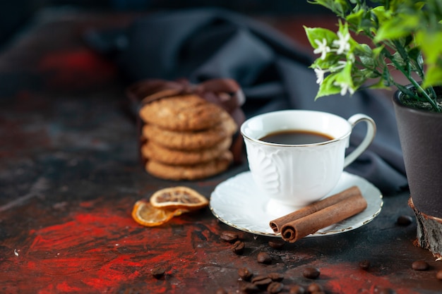 Vista frontal cercana de deliciosas galletas de azúcar y una taza de granos de café, maceta, canela, limas, toalla sobre fondo de colores mezclados oscuros