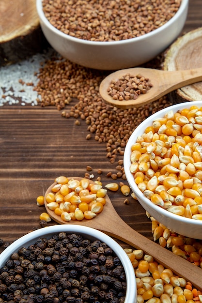 Vista frontal de cereales crudos lentejas granos de arroz y trigo sarraceno con pimienta sobre fondo marrón cena de color comida vegetal comida semilla fresca cocina