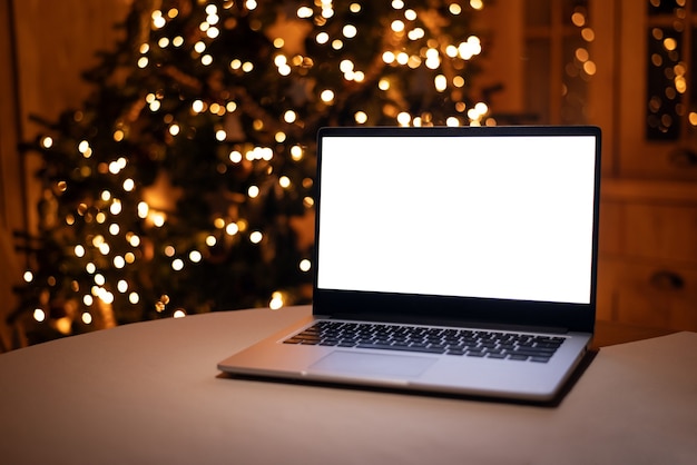 Vista frontal de la computadora portátil de pantalla blanca en casa con luz cálida de árbol de navidad independiente de trabajo remoto