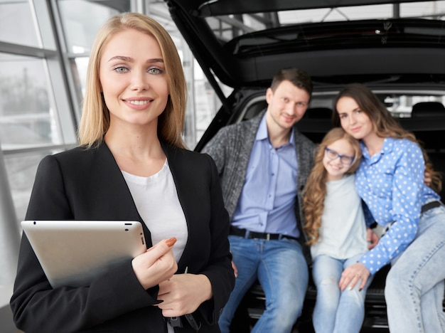 Vista frontal del concesionario de automóviles manteniendo la tableta en el salón del automóvil