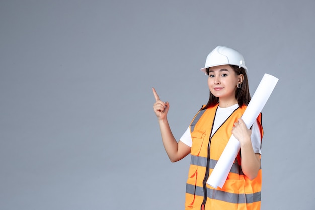 Vista frontal del constructor femenino en uniforme con cartel en sus manos en la pared blanca